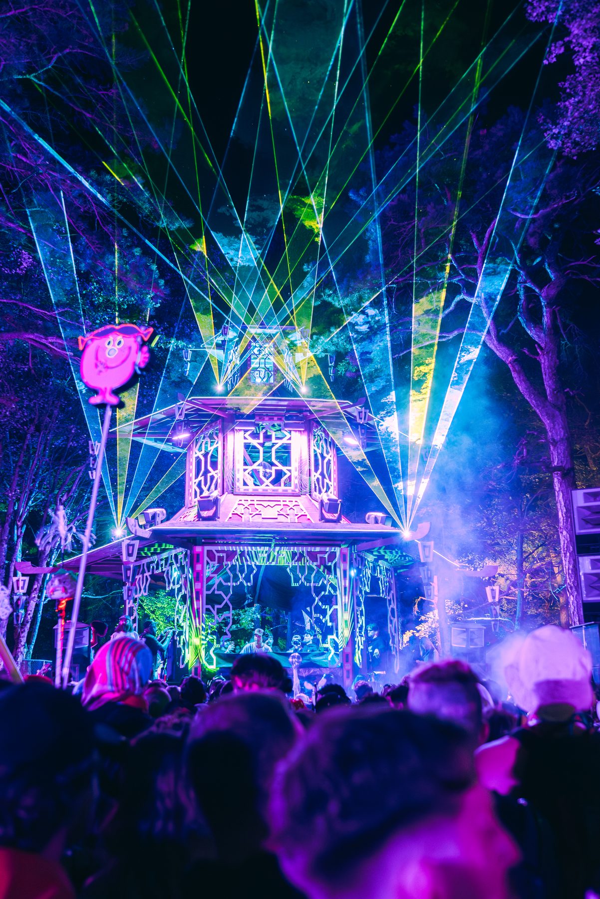 Festival stage art structure lit in purple with lasers over the crowd