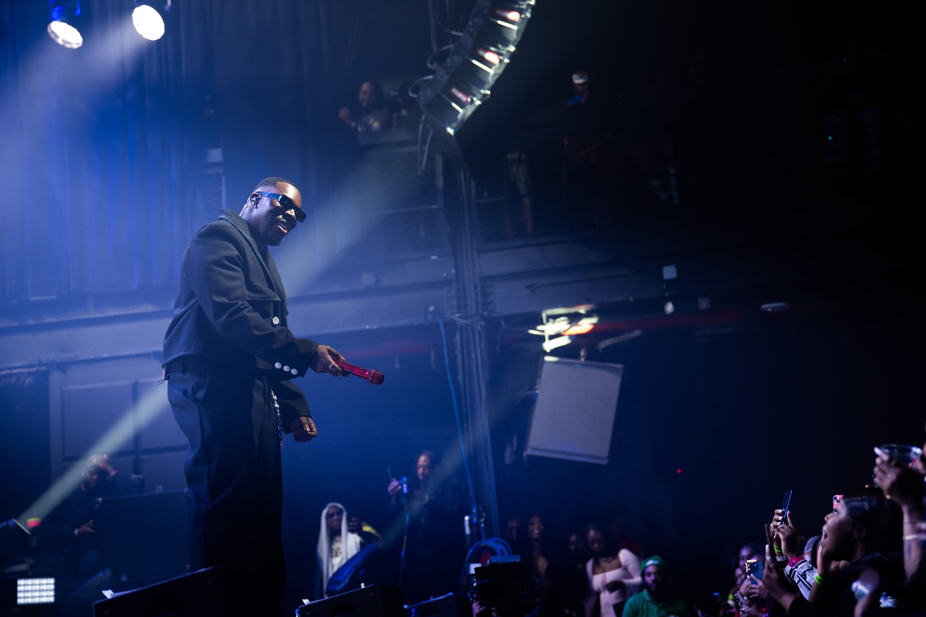Performer on a concert stage under moving lights with a line array overhead